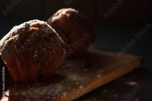 fresh muffins with chocolate lie on a wooden board sprinkled with icing sugar, top view.