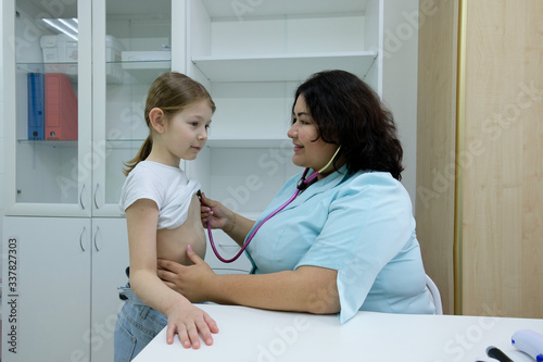 The doctor listens to the patient's heartbeat and breathing with a statoscope in the office. little girl emergency medical examination photo