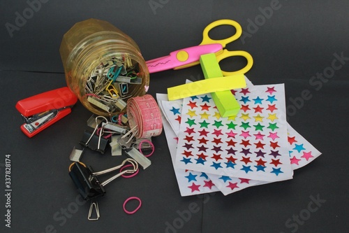 Messy School stationaries & other Equipments on a black background. stickers, staplers, sissors, sticky notes, pins, meassuring tapes and other tools.  photo