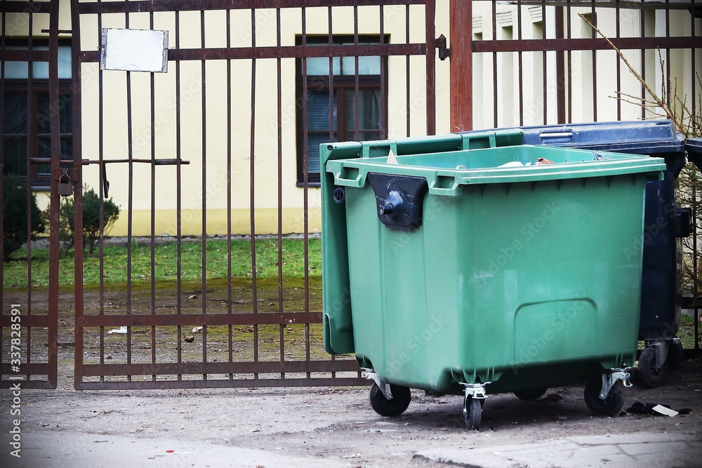 Empty green plastic garbage container standing in front of locked gates Empty green plastic garbage container standing in front of locked gates