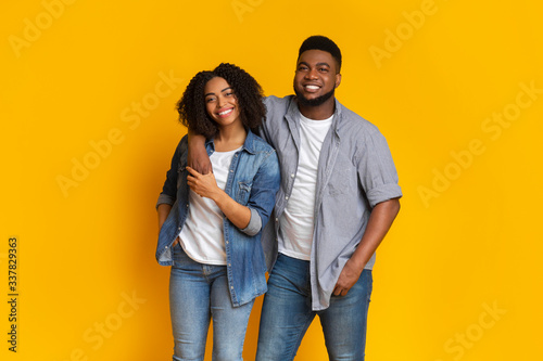 Smiling black man posing with girlfriend over yellow background in studio