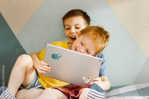two children are sitting at home looking at a computer tablet and laughing