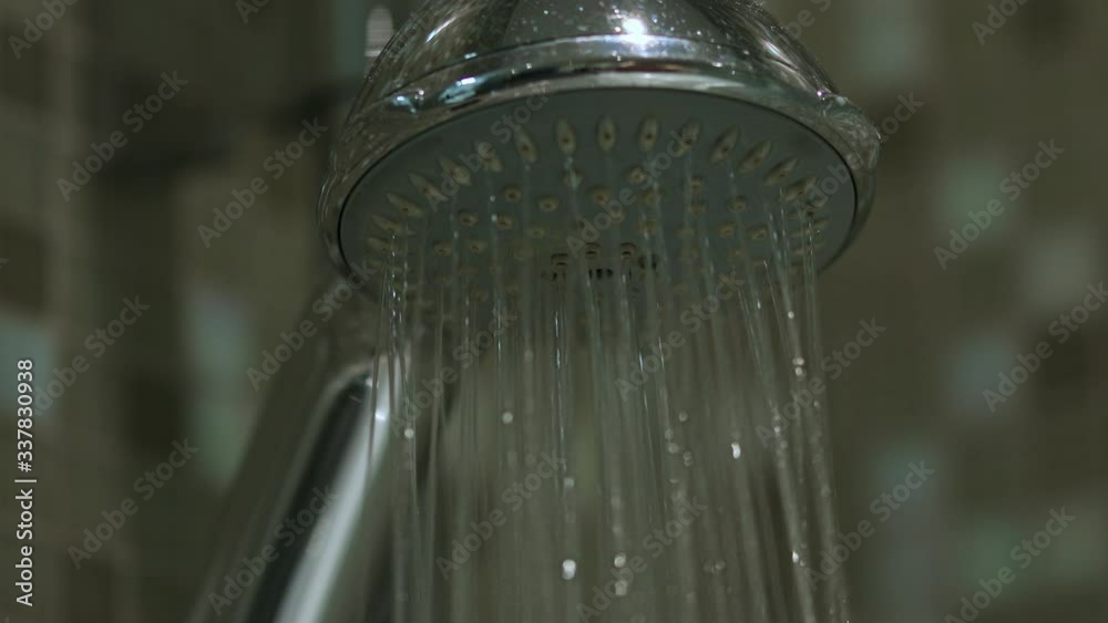 The close view of shower while water is flowing from then in streams and droplets. Bathroom in hotel or spa. Using water for cleaning and refreshing. Hygienic lifestyle.