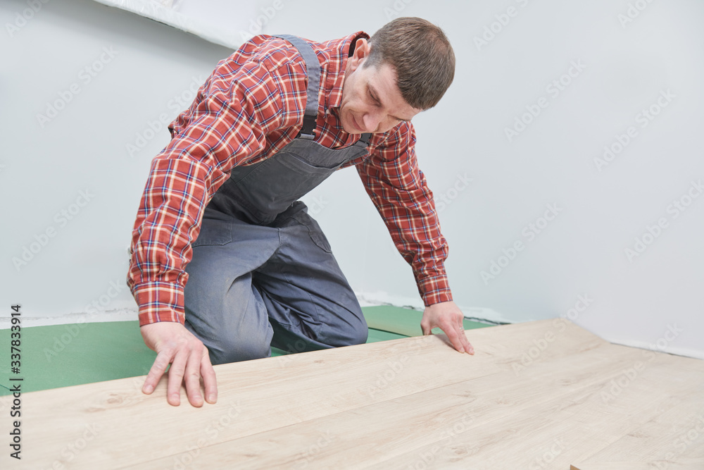 worker laying laminate floor covering at home renovation