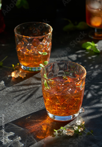 orange summer cocktail with ice on dark background. Shadows of glasses, hard sun light.