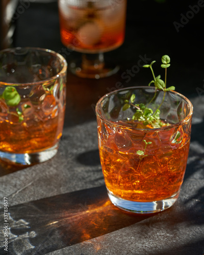 orange summer cocktail with ice on dark background. Shadows of glasses, hard sun light.