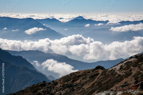 Bands of clouds and mountain intermix in several layers all the way to the horizon from an elevated view point. A barren high altitude terrain in the foreground.