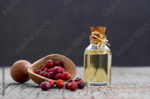 Glass bottle of juniper essential oil with dried juniper berries in wooden spoon on rustic table (juniperus) photo