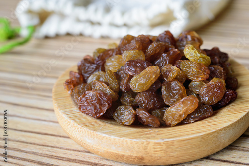 Close up raisins in a plate on a wooden table.