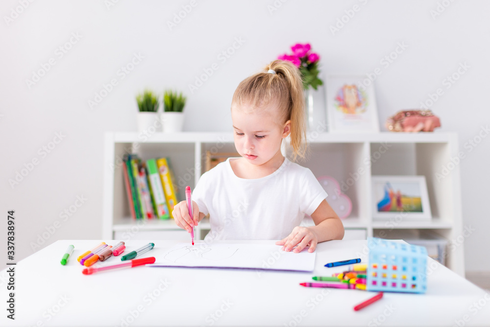 Blonde happy little girl with ponytale drawing and writing lsitting by the white table in light roon. Preschool education, early learning Blonde happy little girl with ponytale drawing and writing lsitting by the white table in light roon. Preschool education, early learning