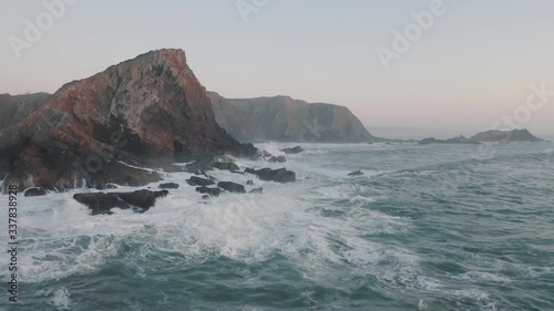 Aerial shot of ocean waves crashing coastline cliff, steep. Sea wave is breaking on the rocks. Aerial drone cinematic footage of beautiful cliffs off the coast of Portugal on the Sunset.