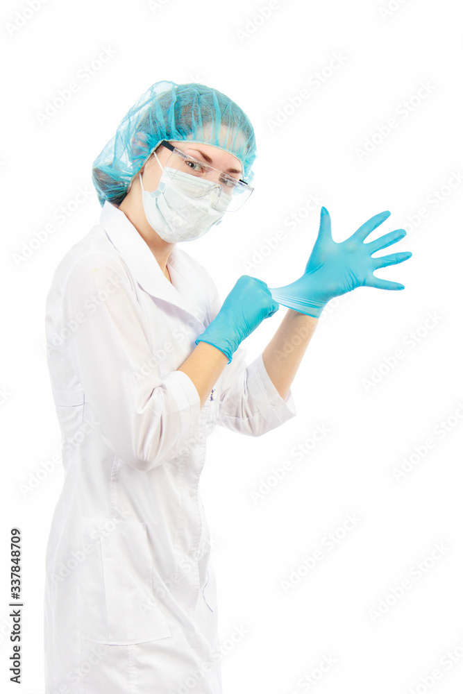 young female doctor in transparent safety glasses cap and white coat pulls colored gloves on his hands on a white background in studio young female doctor in transparent safety glasses cap and white coat pulls colored gloves on his hands on a white background in studio