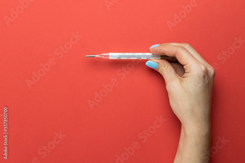 Pandemic background. Womans hands use thermometer to check temperature. Medical equipment on red background. Concept COVID quarantine. Coronavirus Preventive Measures.
