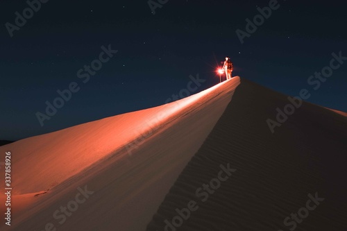 Man with red light standing on sand dune at night