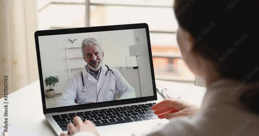 Senior male doctor videoconferencing woman remote patient consulting about corona virus pandemic during telemedicine video call in conference virtual webcam chat app. Over shoulder laptop screen view. Senior male doctor videoconferencing woman remote patient consulting about corona virus pandemic during telemedicine video call in conference virtual webcam chat app. Over shoulder laptop screen view.