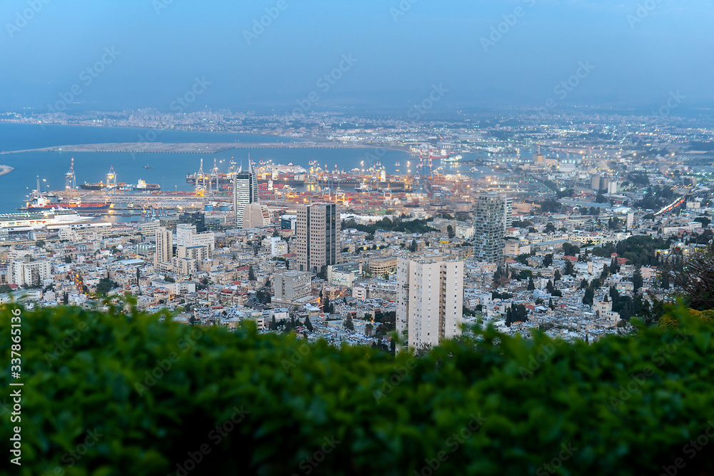 Evening view of Haifa town from Bahai Gardens in Israel with blurred green bushes on the foreground