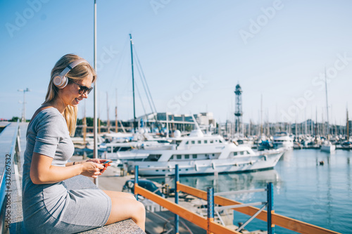 Cheerful woman listening to music and using smartphone in harbor