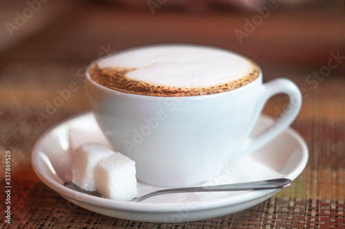 Cup of coffee on a wooden table with two pieces of shugar