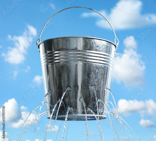 Leaky bucket with water against blue sky
