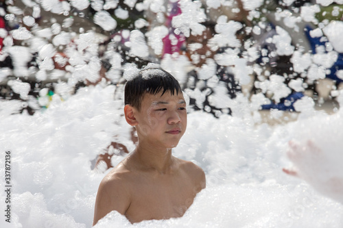 Close-up: A cute Asian boy smiles in the Foam Party at the outdoor pool. 