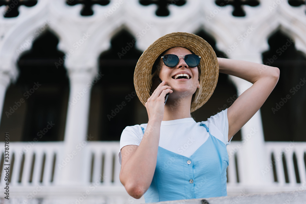 Smiling Caucasian tourist making international cellphone conversation with friend and talking about summer vacations, happy female traveler in trendy sunglasses calling via mobile technology