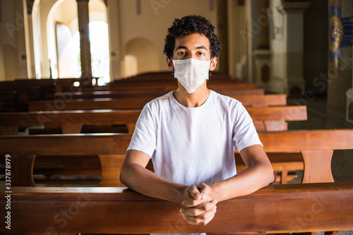 Jovem reza em igreja utilizando máscara de proteção.  photo