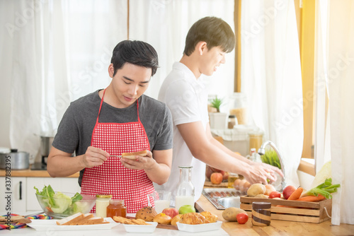 Happy young Asian homosexual gay couple cooking breakfast meal together in the kitchen. Handsome guy LGBTQ lover enjoy with romantic lifestyle at home. Same-sex marriage and LGBT relationship concept.