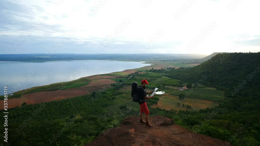 man traveler with backpack looking at the map on the edge of cliff man traveler with backpack looking at the map on the edge of cliff
