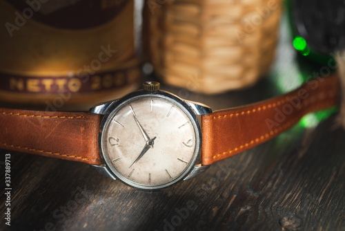 Retro wrist watch with white dial and brown leather strap, lying on rustic wooden table