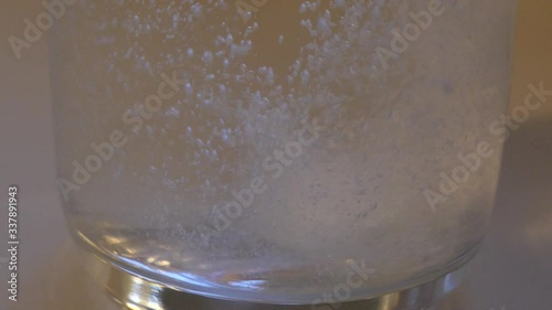 Slow motion close up of white tablet dropping into clear drinking glass of water and dissolving into a fizz cloudy liquid. photo