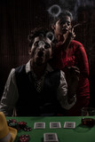 An young and attractive Indian brunette couple in vintage suits smoking in a casino poker table in brown textured copy space background. Gambling and addictive lifestyle.