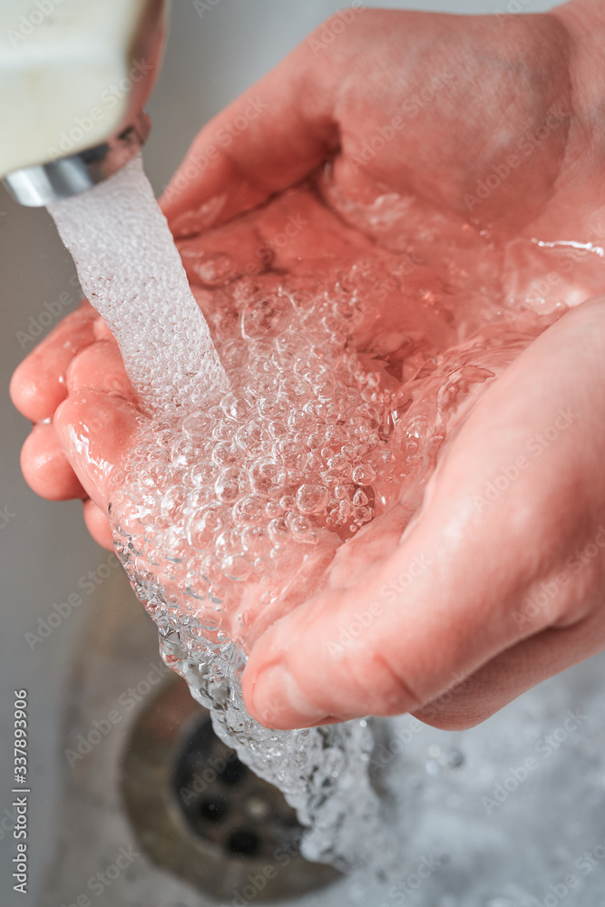 Fototapeta premium Hands holding water with big bubbles and dropping under the faucet while washing with light reflections on the palms for coronavirus prevention