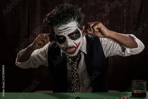 Portrait of an Indian man in Halloween costume showing scary facial expression in front of a casino poker table. Cosplay photography.