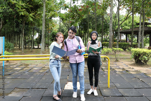 Young asian malay chinese man woman outdoor park walk stand study talk discuss point laptop file book backpack mingle