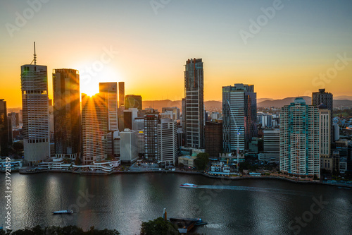 Brisbane city skyline view with sunset sun streaking light beams with boat crossing the river