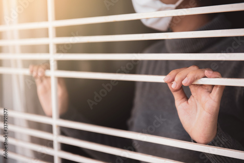 Stay at home. Corona virus or Covid-19 concept. Woman in protection mask standing and looking through the window in her home with prevent infection of pandemic. Quarantine at home.