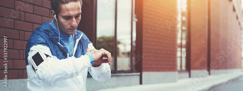 Young athlete in blue windrunner sitting on the street adjusting running program for his early morning workout using smart watches on his hand photo
