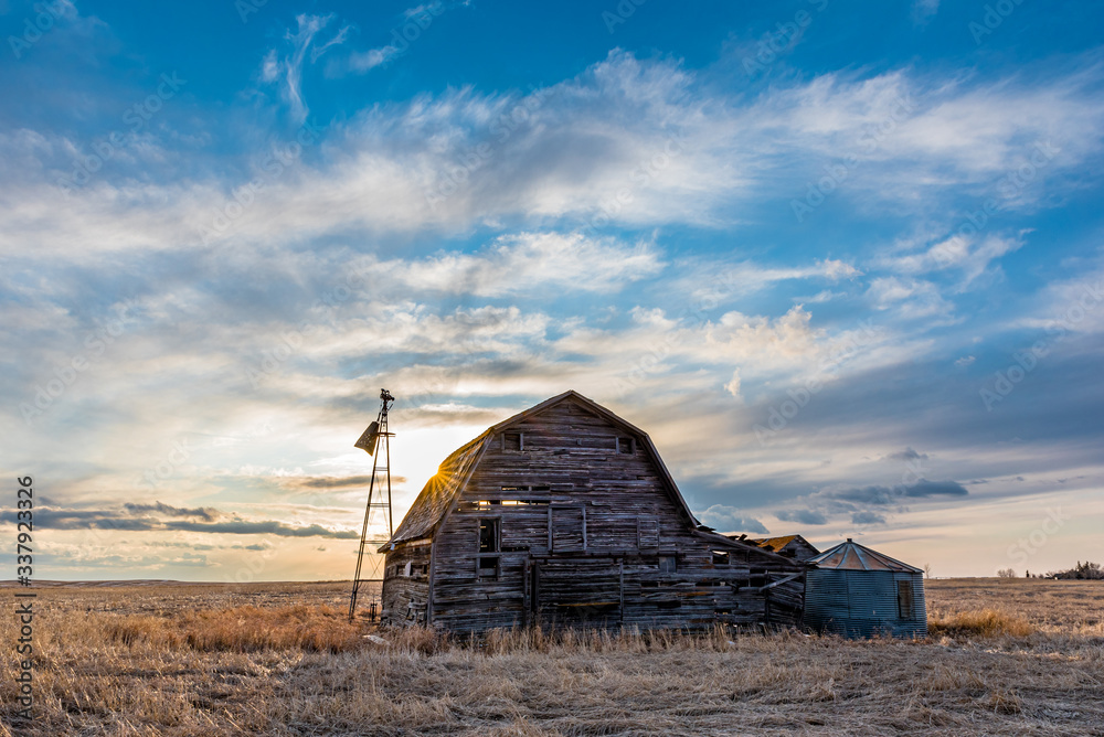 Sunset over a vintage wooden barn, bins and windmill in a Saskatchewan, Canada 