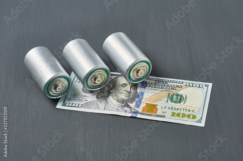 Old used batteries and banknote of one hundred dollars on dark concrete desk. Recycling concept. Save environment. Cost, purchase or sale of electricity