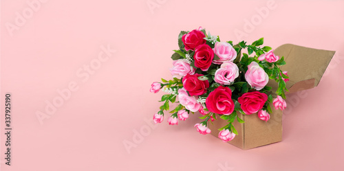 Moving single cardboard box with a bouquet of red and pink beautiful bright roses on a pink background as a gift for a wedding, Valentine's day or March 8 to a woman: flower shop concept, delivery © Leila