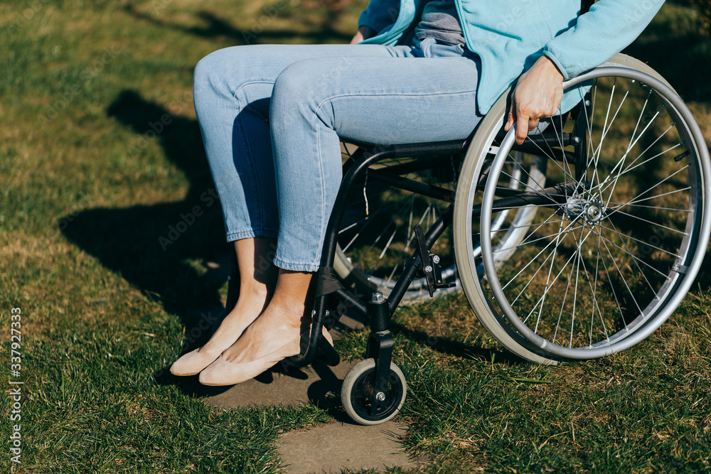 Obraz premium Close up of a young woman in a wheelchair while walking in a park on a sunny day. Recovery and healthcare concepts.