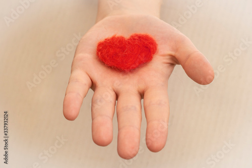 Close-up of an open palm on which lies a red heart made of felted wool