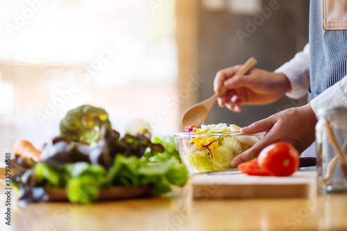 Closeup image of a female chef cooking and holding a bowl of fresh mixed vegetables salad in kitchen