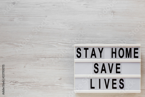 'Stay Home Save Lives' words on a lightbox on a white wooden background, top view. Overhead, from above, flat lay. Copy space.