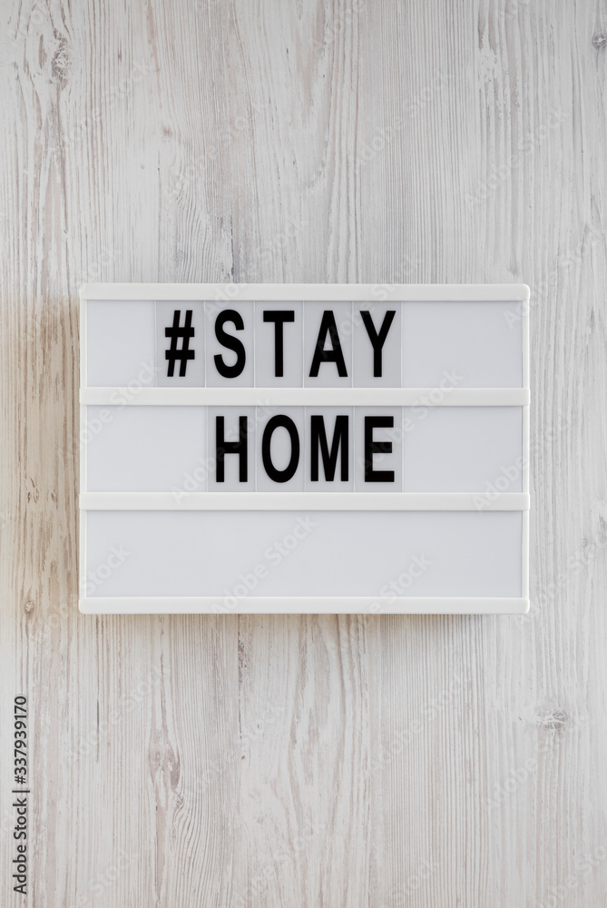 'Stay home' words on a lightbox on a white wooden surface, top view. Overhead, from above, flat lay.