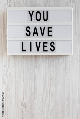 'You save lives' words on a lightbox on a white wooden surface, top view. Overhead, from above, flat lay. Copy space.
