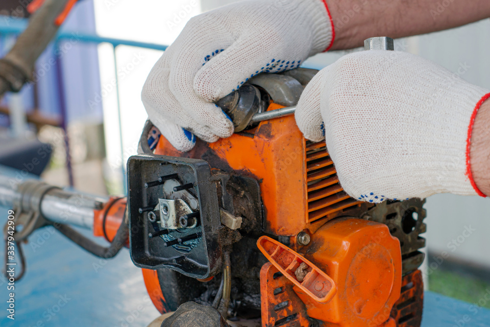 a master in working gloves repairs the engine of the old gas trimmer with a screwdriver removes the tip of the high-voltage wire from the spark plug