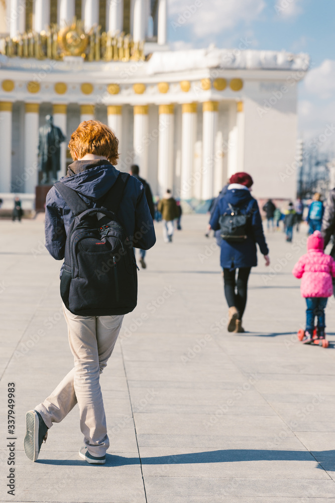 Obraz premium April 2019 - Moscow Russia - a young red hair man is staying in front of main pavilion building at all Russian exhibition center park and looking at his mobile phone
