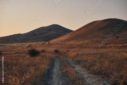 road in the field against the background of mountains and blue sky