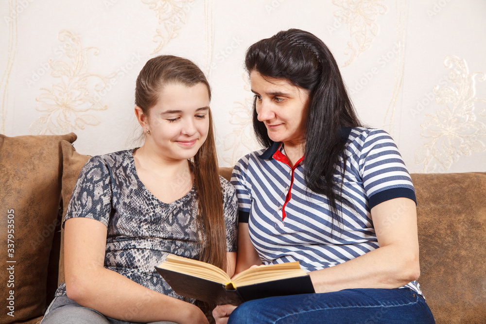 mom and daughter are reading a book while sitting on the sofa mom and daughter are reading a book while sitting on the sofa